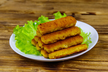 Fried fish fingers on a plate with lettuce on wooden table