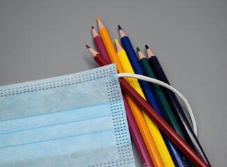 Handful of colored pencils inside the elastic rubber of a surgical mask.