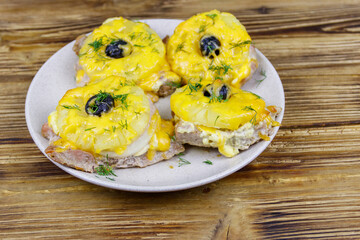 Pieces of baked pork with pineapple, cheese and olive on a wooden table