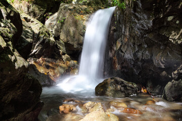 Mountain waterfall flows among green forest and runs down the beautiful gray stones. Amazing summertime wallpaper background.