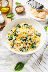 Pasta fettuccine with spinach  in creamy cheese sauce on a white wooden background.