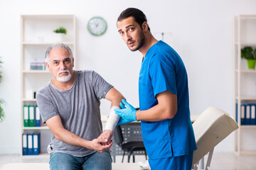 Young male doctor and old patient in first aid concept