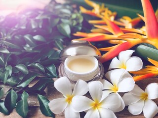 Obraz na płótnie Canvas Facial cosmetic cream container and Heliconia flower,Frangipani flowers,on old wood plank.Rustic still life,soft dark tone,dimly light,with lens flare,free space for your text design or your products.