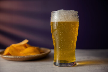 Glass of Beer and plate with Potato Chips on Table. Drinking Beer at Home or Cafe