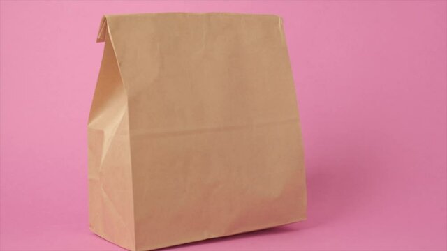 Hand holding brown transparent empty paper takeaway food bag isolated on pastel pink background. Packaging template mockup. Delivery service concept. Copy space ad space