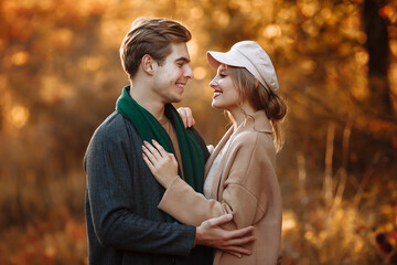 guy and girl are embracing and smiling while looking at the camera, a beige cap and a green scarf, autumn. date of a happy and loving couple