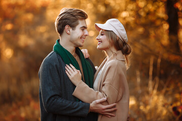 Fototapeta premium guy and girl are embracing and smiling while looking at the camera, a beige cap and a green scarf, autumn. date of a happy and loving couple