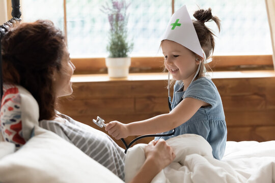 Daughter wear medical cap hold stethoscope imagines herself like doctor listen heartbeat treats caring about mother heart health. Playtime with kid, cardiologist profession in future, vocation concept