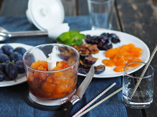 Dark background with a blue ripe plum on a blue napkin. The process of making creamy juice from natural plums or smoothies using a mixer.