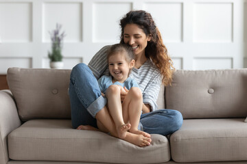 Mommy cuddle little daughter tickles her feels overjoyed, spending time together at home. Nanny and...