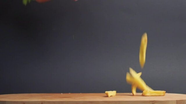 Beautiful Slow-motion Shot Of Falling Fries And A Sandwich From Above. Wooden Table. Gray Background.