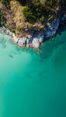 Vertical orientation aerial view. Top view of turquoise sea water washes the rocky shore in Thailand. Landscape background