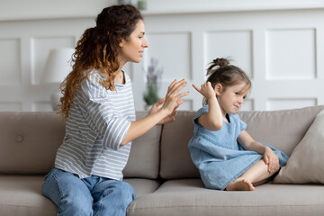 Fototapeta na wymiar Single mother and little kid sit on couch at home, parent scolds preschool daughter teaches naughty mischievous child. Concept of punishment, bad behaviour misbehave of infant, upbringing difficulties