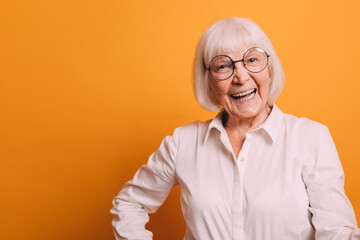Image of happy old woman with light short hair wearing white blouse holding her arms on hips and...