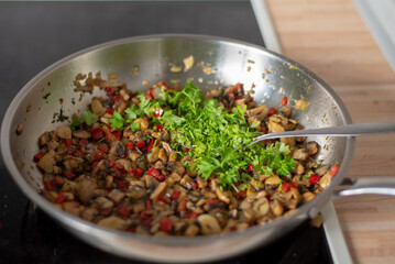 fried paprika and onions on a hot frying pan sprinkled with parsley, preparing a meal at home