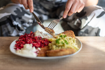 the person holds a fork and knife in her hand, in front of her, there is a homemade meal on the plate