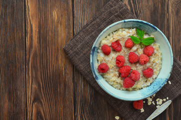 Delicious and hearty breakfast oatmeal porridge with raspberries in a beautiful ceramic bowl. The concept of healthy food, diet, organic nutrition and lifestyle. Space for text and design