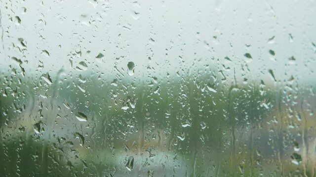 Rain drops sliding slow on window glass in rainy day, medium closeup shot