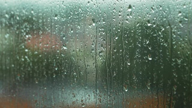 Rain drops sliding slow on window glass in rainy day, de-focused city in background,medium closeup shot