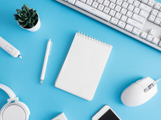 top view of office desk table with notebook, plastic plant, smartphone and keyboard on blue table background, graphic designer.