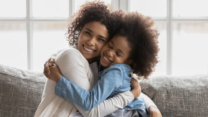 Obraz premium Portrait of sweet emotional african american bonding two generations family cuddling on comfortable sofa at home. Affectionate caring mixed race mommy showing sincere feelings to small daughter.