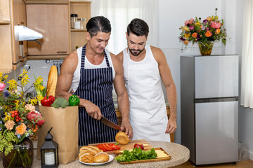 Lovely gay couple is helping each other to prepare vegetables for healthy breakfast in the kitchen at home