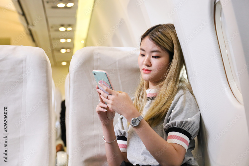 Wall mural asian woman travels sitting comfortably in the aircraft while using mobile phone copy space