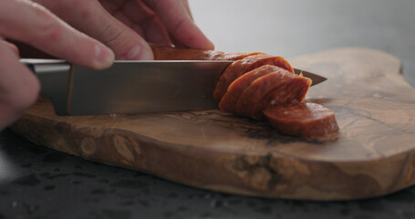 slicing chorizo sausage on olive wood board closeup