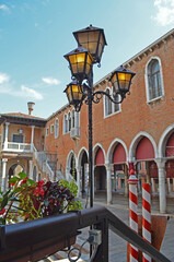 
glimpse of a typical Venetian building with a small metal lamppost in the foreground with lights on