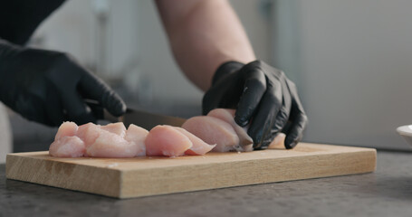 Man hands in black gloves cutting chicken fillet on oak board - Powered by Adobe