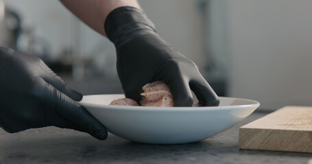Man hands in black gloves marinating chicken fillet in white bowl