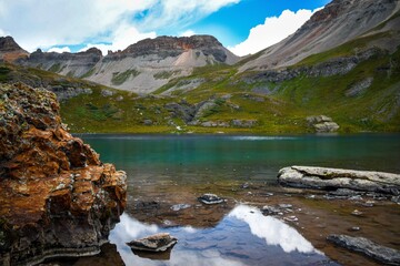 Incredibly blue alpine lake in the mountains of Colorado. Turquoise water and beautiful scenery with rocks in the water, peaks, blue skies, and clouds.