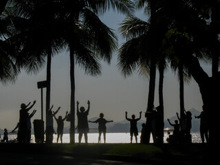 Small group of people in silhouette, arms raised, facing water