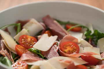 Salad with prosciutto, tomato, arugula leaves and parmesan cheese in white bowl closeup