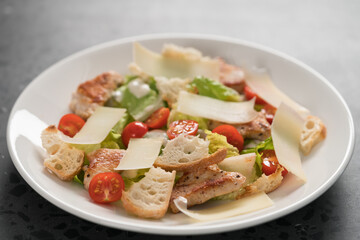 Fresh caesar salad with chicken and cherry tomatoes in white bowl