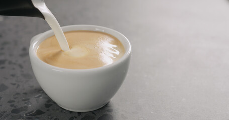 Pour steamed milk making cappuccino in white cup on concrete background
