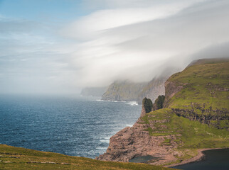 Fototapeta na wymiar Faroe Islands Traelanipa the slaves rock cliff is seen rising over the ocean next to lake Sorvagsvatn. Clouds and blue sky during suommer on the island vagar in the Faroe Islands.