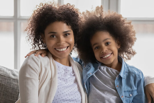 Head Shot Portrait Of Happy African American Woman Resting With Adorable Small School Aged Sincere Kid Daughter. Smiling Multigenerational Biracial Family Looking At Camera, Enjoying Tender Moment.