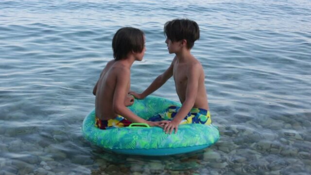 Children, preteen boys, playing on the beach with inflatable ring, having fun in the water