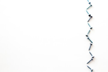 Flat lay shot of screws forming a zigzag line on white surface with space for your text
