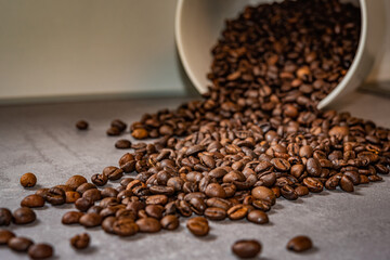 Brown coffee beans on a grey surface close up falling out of a white bowl