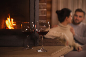 Lovely couple resting near fireplace, focus on glasses with red wine