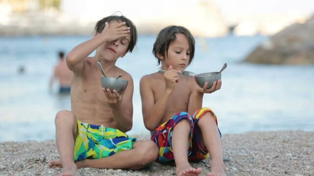 Cute boys, children, eating spaghetti on the beach, enjoying dinner outdoors
