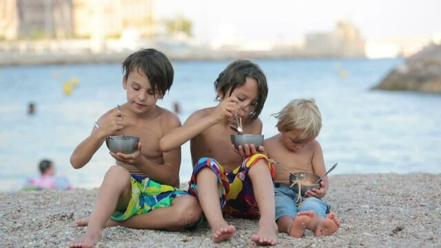 Cute boys, children, eating spaghetti on the beach, enjoying dinner outdoors