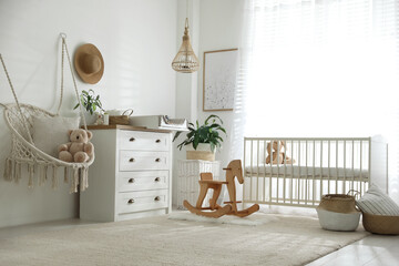 Chest of drawers with changing tray and pad near comfortable cradle in baby room. Interior design