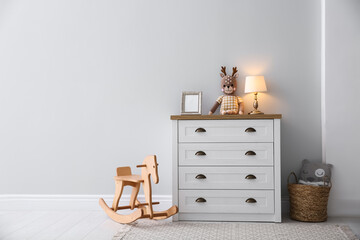 Modern white chest of drawers near light wall in child room, space for text. Interior design