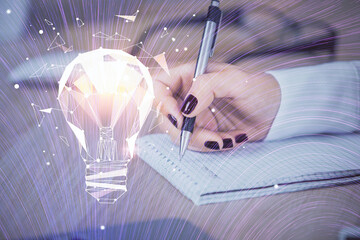 Bulb hologram over hands taking notes background. Concept of idea. Double exposure