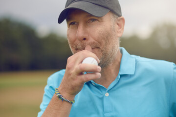 Middle-aged male golfer contemplating his shot staring down the fairway with a golf ball in his...