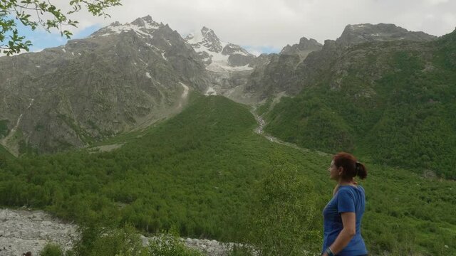 Back view of woman in blue t shirt stands in reen valley and looks at bare rocks. Admiring nature.