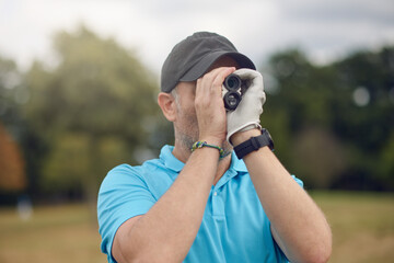 Golfer using a rangefinder to measure the distance to the hole holding it to his eye as he peers...